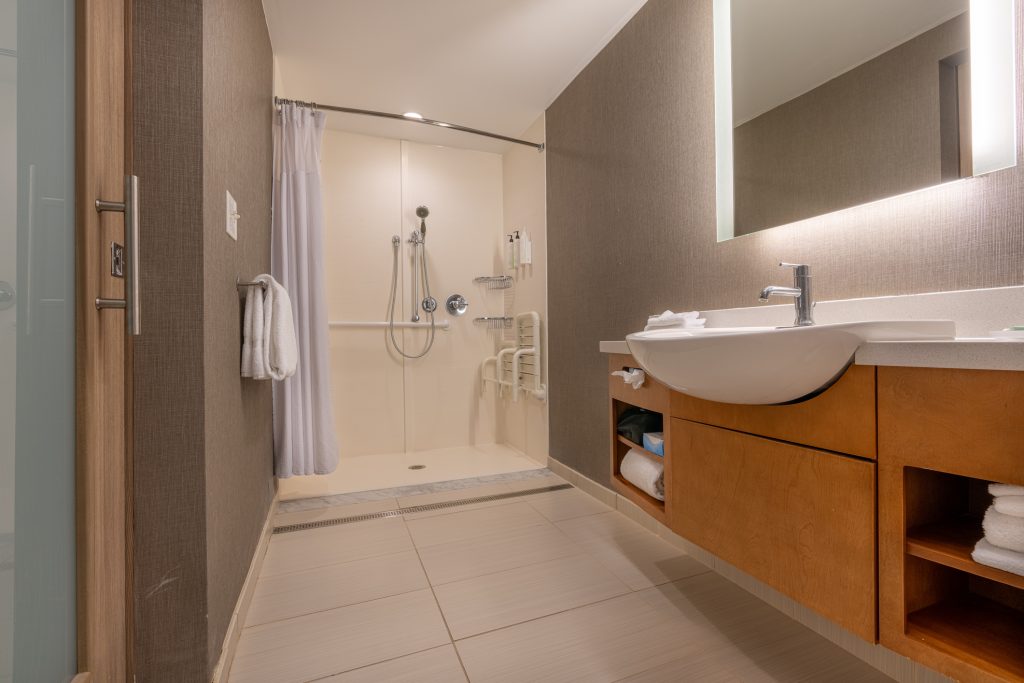 Wheelchair accessible hotel bathroom shower with tile floor and walls.